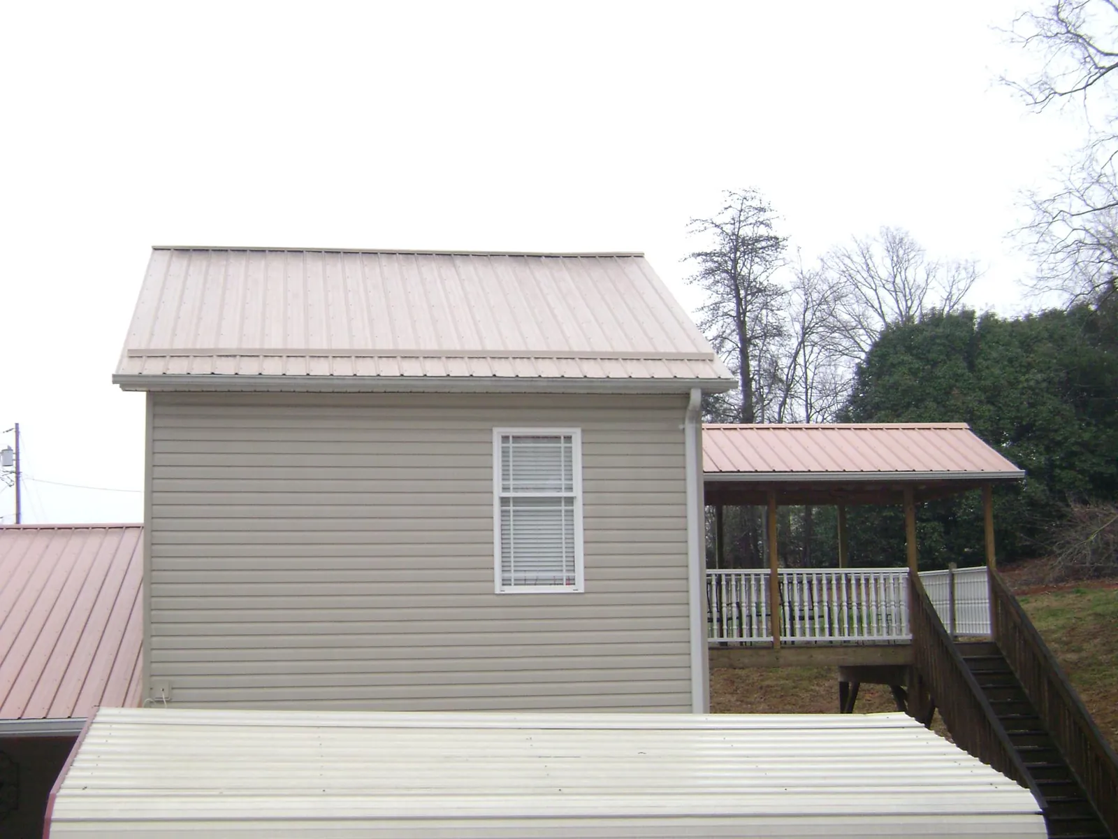 Tan metal roofs on a two story addition and attached porch, from a Roof Replacement job in Petersburg